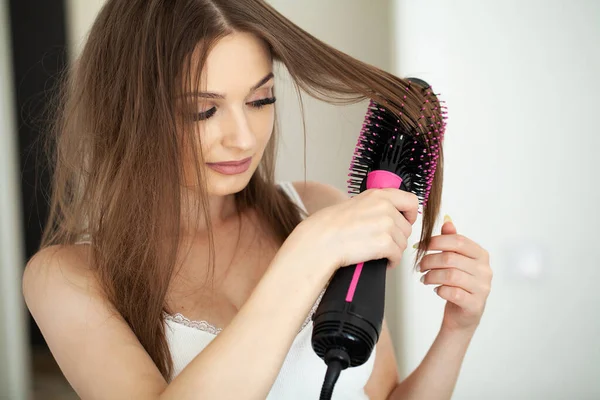 Woman with long hair and healthy skin drying her hair while standing in bathroom