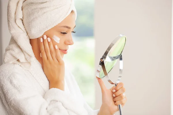 浴室里头戴毛巾的女人看着镜子 摸着镜子里的脸 享受青春和水合 — 图库照片