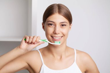 Güzel genç bir kadın dişlerini banyoda fırçalıyor..