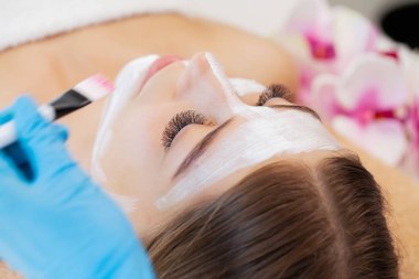 Yüzünde kil maske olan çekici ve komik bir kadın.