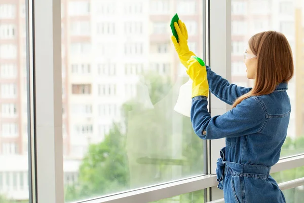 A woman in yellow gloves washes windows in an office center.