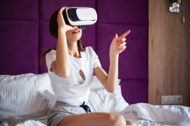 Yatak odasında sanal gerçeklik gözlüğü takan genç bir kadın..