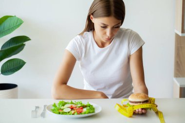 Güzel genç bir kadın mutfakta hamburger ya da taze salata yemeye karar verir.