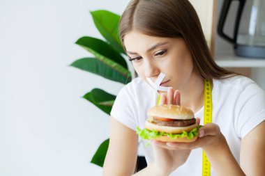 Hamburger yemek isteyen bir kadının portresi, ama ağzı bantlı..