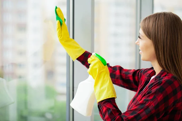A woman in yellow gloves washes windows in an office center.