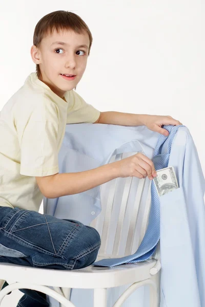 Handsome young lad gets money from the shirts hanging on a chair — Stock Photo, Image