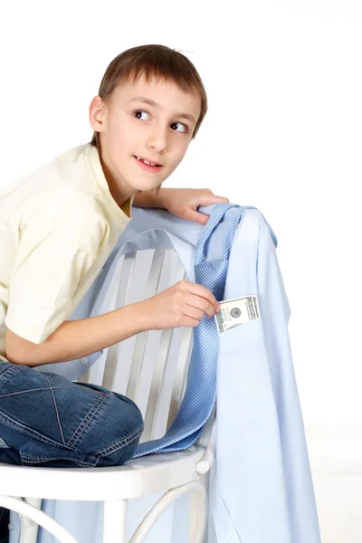 Handsome young kid gets money from the shirts hanging on a chair — Stock Photo, Image