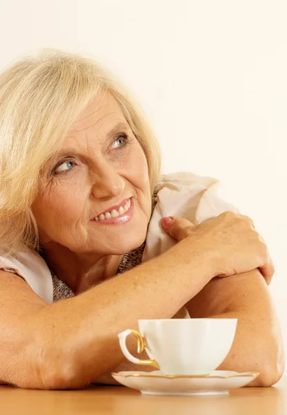 Old woman with coffee on a beige — Stock Photo, Image