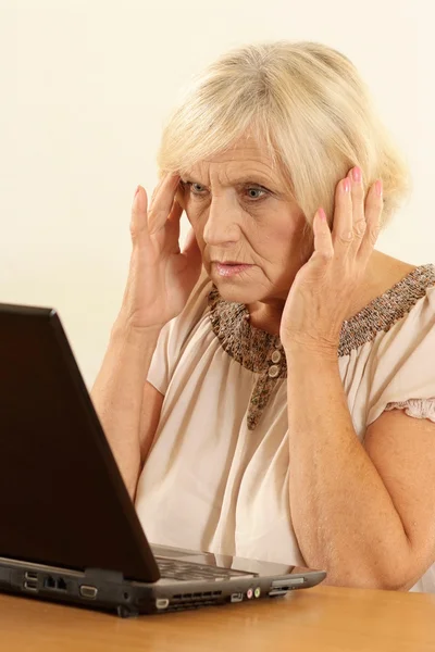 Old woman with a laptop on a beige — Stock Photo, Image