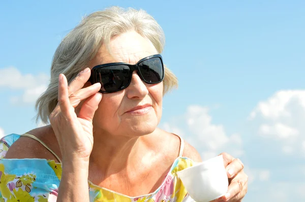 Elderly woman with cup on sky background — Stock Photo, Image