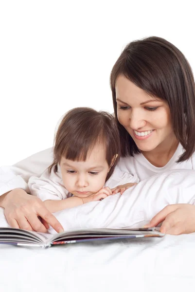 Hermosa mamá caucásica y su hija tumbada en la cama con un libro —  Fotos de Stock