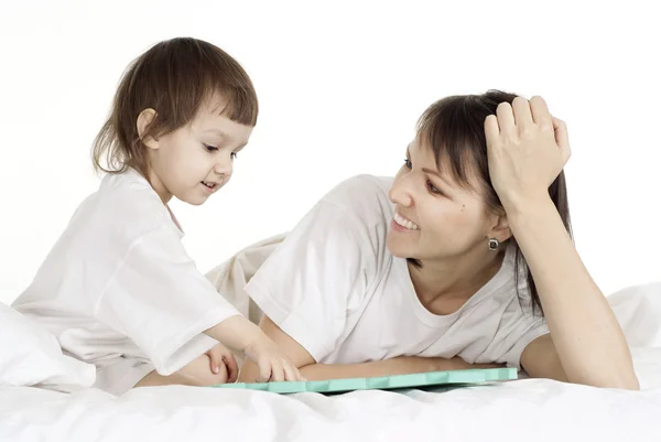 Beautiful caucasian mama and daughter lying on the bed with a book — Stock Photo, Image