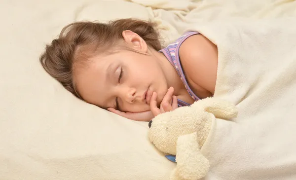 Linda niña durmiendo con un juguete en su cama — Foto de Stock