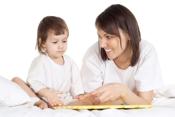 Beautiful caucasian mama and daughter lying on the bed with a book — Stock Photo, Image