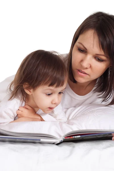 Beautiful caucasian mama and daughter lying on the bed with a book — Stock Photo, Image