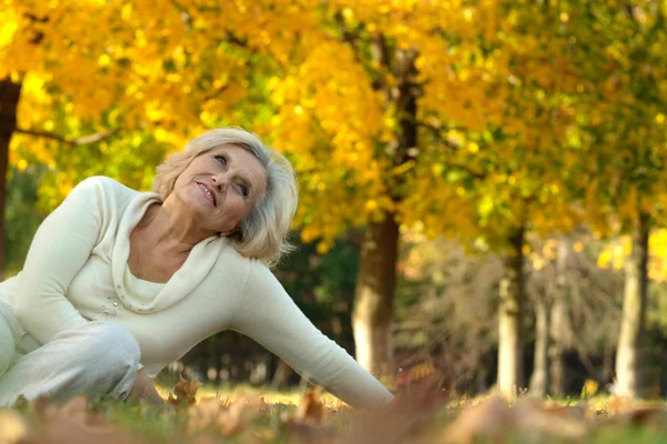 Alte Frau sitzt auf den Herbstblättern — Stockfoto