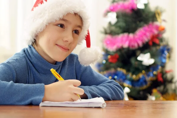 Adolescente muito caucasiano em um chapéu de Pai Natal desenha — Fotografia de Stock