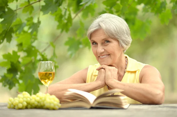 Mulher velha bebendo vinho e lendo um livro — Fotografia de Stock