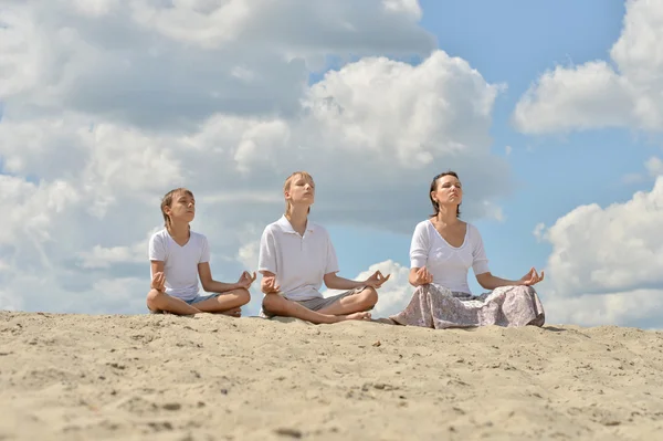 Mutlu aile bir kum üzerinde oturan ve yoga yaparken — Stok fotoğraf