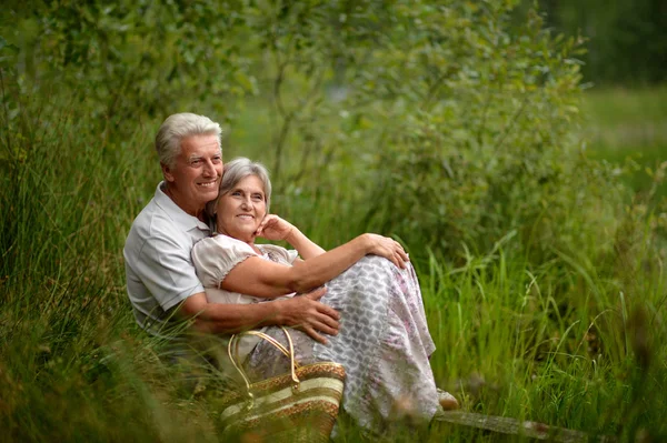 Oude paar zitten in het gras in de buurt van het meer — Stockfoto