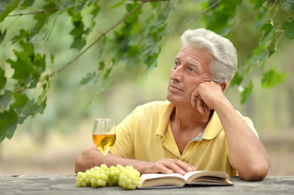 Old man drinking wine and reading a book — Stock Photo, Image