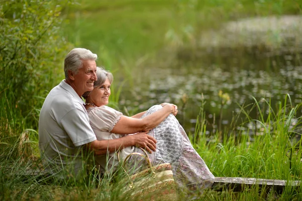 Old couple sitting in the grass near the lake — Stock Photo, Image