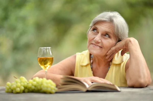 Gammal kvinna dricker vin och läsa en bok — Stockfoto