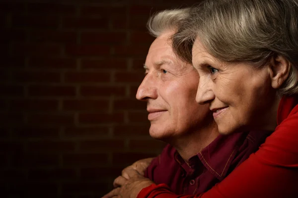 Casal idoso em vermelho em um fundo de um tijolo — Fotografia de Stock