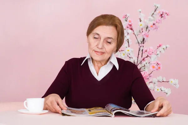 Beautiful Caucasian aged woman sitting with a magazine — Stock Photo, Image