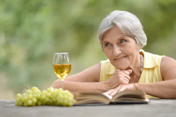 Пожилая женщина с вином и книгой — стоковое фото