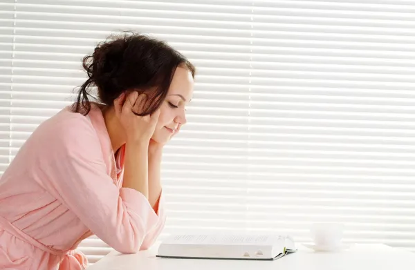 Ein hübsches kaukasisches Mädchen sitzt mit einem Buch am Tisch — Stockfoto