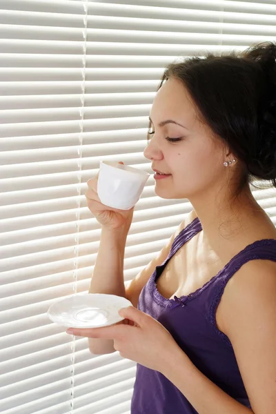 Ein schönes kaukasisches Mädchen, das neben einem Fenster mit einer Tasse steht — Stockfoto