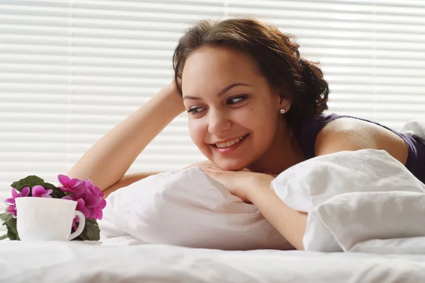 Schöne hübsche Frau, die in einem Beet aus Blumen und Tasse liegt — Stockfoto