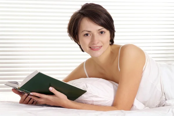 Mujer leyendo un pastel en una cama —  Fotos de Stock