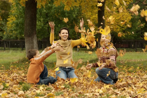 Mom and her children throwing autumn leaves — Stock Photo, Image