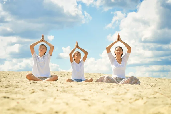 Mutlu aile bir kum üzerinde oturan ve yoga yaparken — Stok fotoğraf