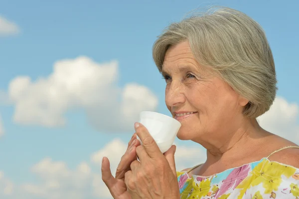 Ältere Frau mit Tasse auf Himmelshintergrund — Stockfoto