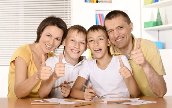 Glückliche Familie zeichnet gemeinsam am Tisch und zeigt Daumen hoch — Stockfoto