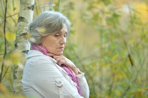 Porträt einer traurigen alten Frau, die an einem Baum steht — Stockfoto