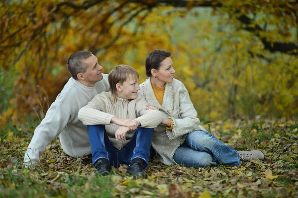 Happy family in park sitting on yellow leaves — Stock Photo, Image