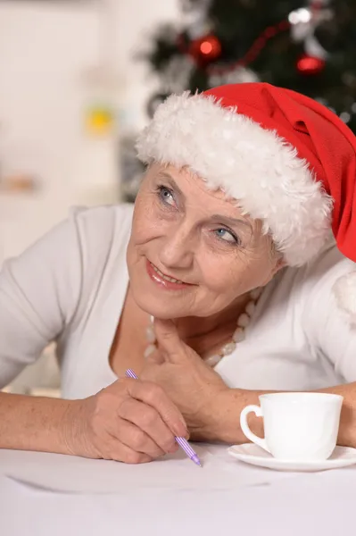 Glückliche ältere Frau mit Weihnachtsmütze, die einen Brief schreibt — Stockfoto