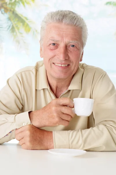 Ładny stary człowiek pije kawę przy stole — Zdjęcie stockowe