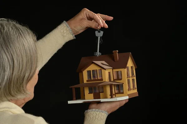 Старшая женщина держит миниатюрный дом и ключ — стоковое фото