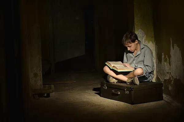 Lonely little boy with book   in a dark cellar — Stock Photo, Image