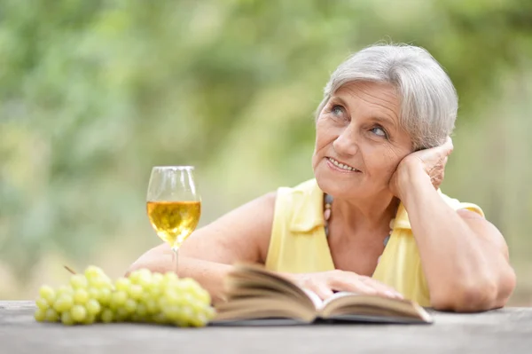 Elderly woman with wine and book — Stock Photo, Image