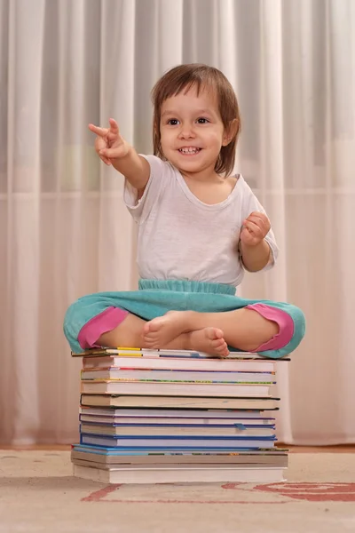 Söt liten flicka sitter på böcker — Stockfoto