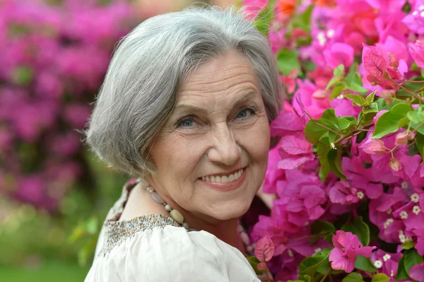 Older woman on walk with pink flowers — Stock Photo, Image