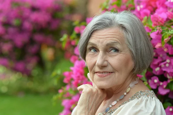 Mulher mais velha em passeio com flores rosa — Fotografia de Stock