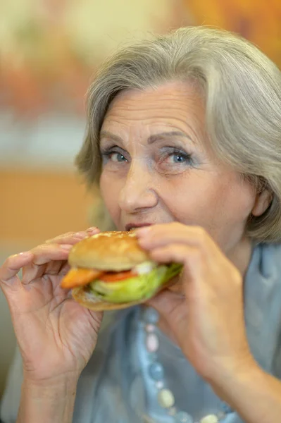 Senior woman eating hamburger — Stock Photo, Image