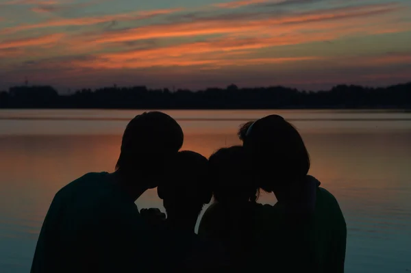 Familjen nära floden mot solnedgången — Stockfoto